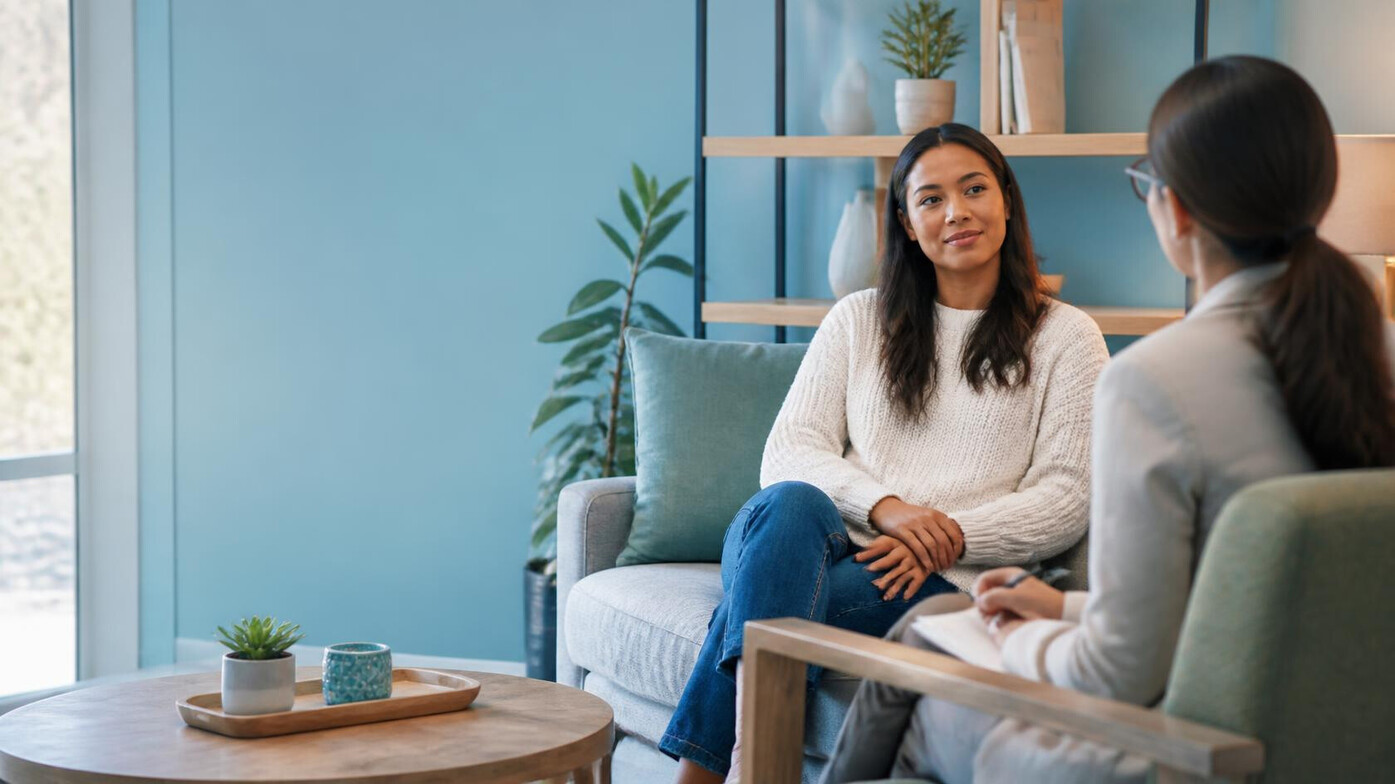 A psychotherapist talks with an adult client during a calm counselling session in a bright, welcoming clinic.